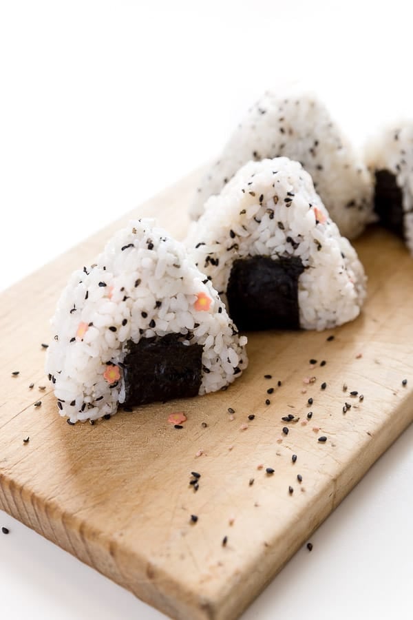 Three Japanese rice balls on a plate scattered with black sesame seeds.