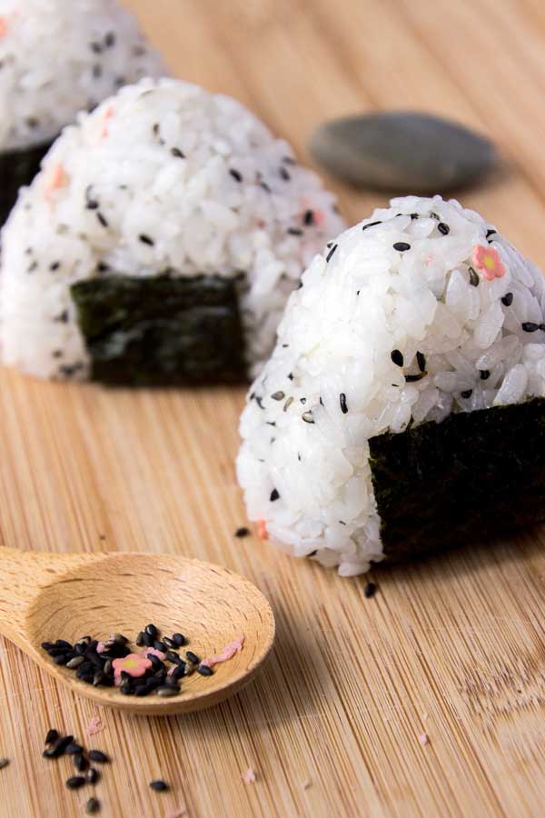 Onigiri rice triangles on a board next to a spoon full of rice seasoning.