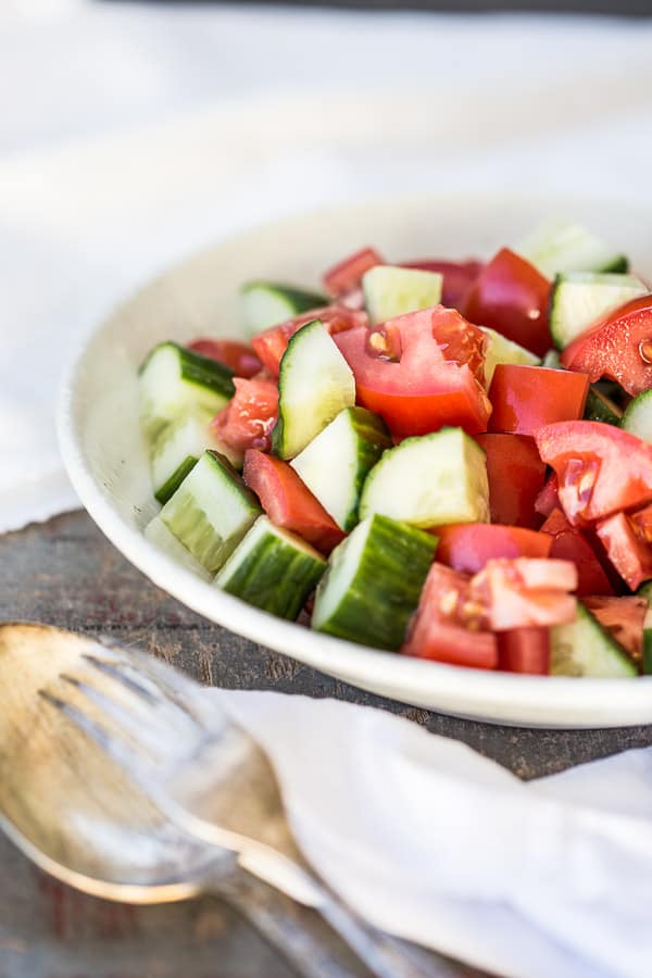 Chopped cucumber and tomato in a bowl next to serving spoons. 