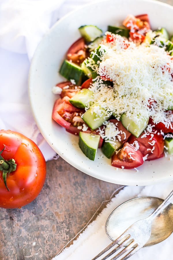 A colourful bowl of salad next to a juicy red tomato. 