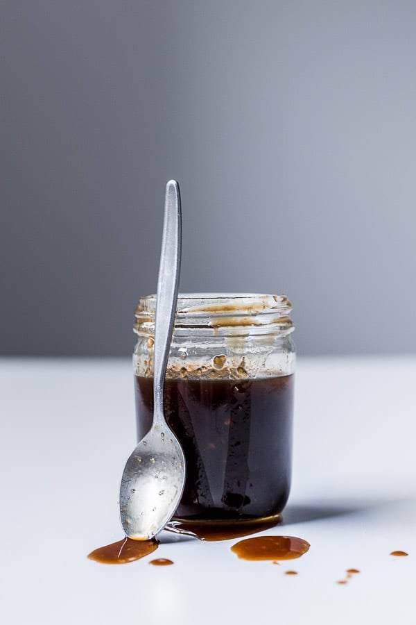 Yakisoba sauce in a small jar, with a spoon and splatters of sauce on the table.