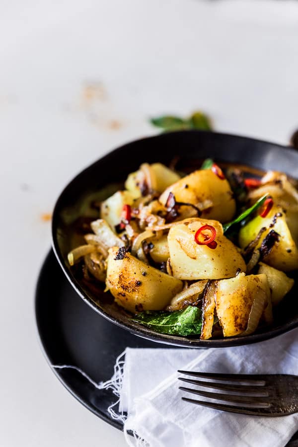 A bowl of spicy potatoes garnished with curry leaves and fresh chilli.