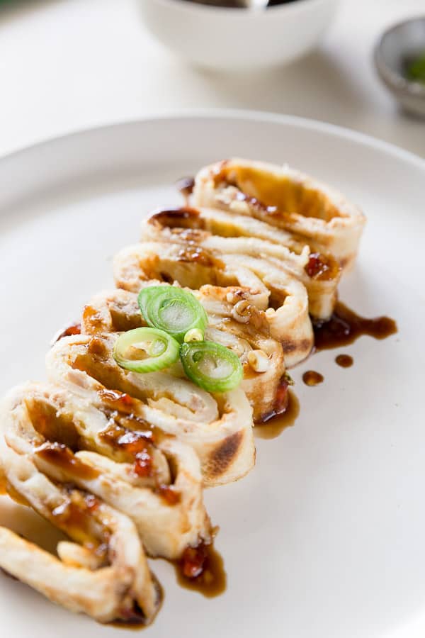 Slices of tuna and egg dan bing crepe on a plate, drizzled with soy sauce and sweet chilli sauce.