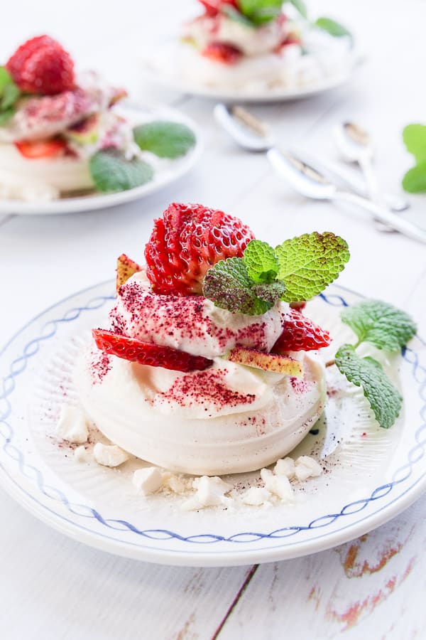 A close up shot of a mini meringue nest topped with whipped cream, strawberries and mint. 