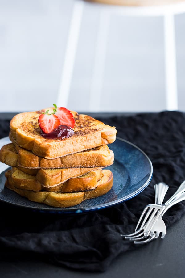 A stack of fluffy french toast on a plate with fresh strawberries. 