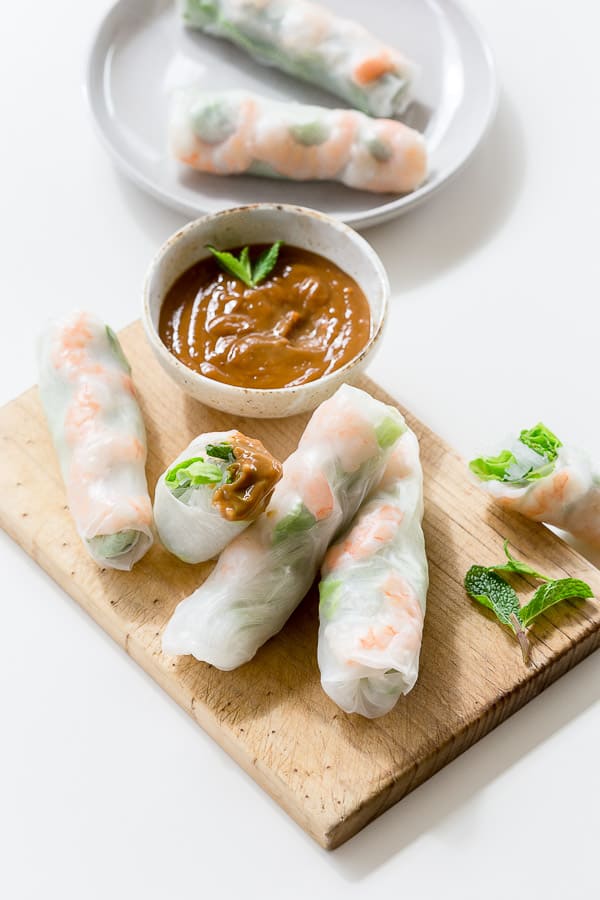 Vietnamese rice paper rolls on a chopping board next to a bowl of dipping sauce. 