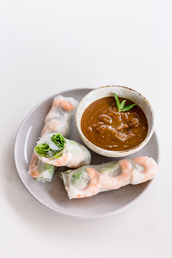 A bowl of rice paper roll dipping sauce with three cold rolls on a plate. 