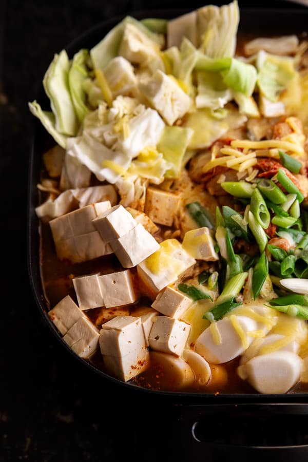 A close up of Korean army stew ingredients including tofu, rice cakes (tteok) and sliced green onions.