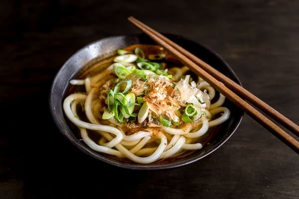 Udon noodle soup in a bowl garnished with spring onion, katsuoboshi (bonito flakes) and Japanese chilli flakes.