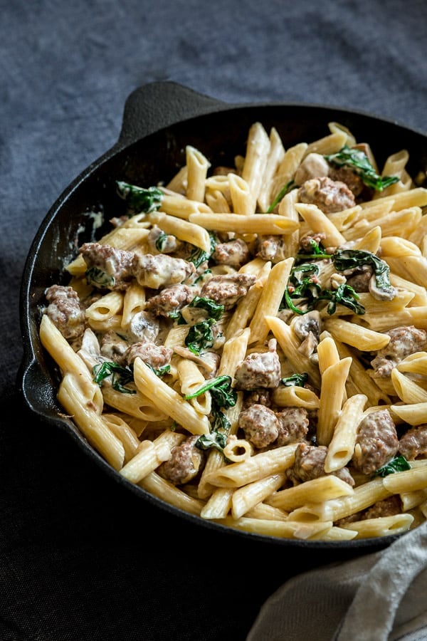 Close up shot of cooked pasta in a creamy sauce with spinach and Italian sausages.