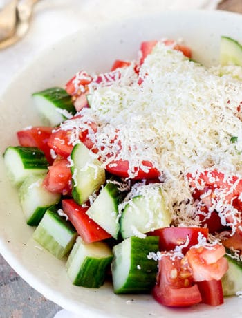 Shopska salad in a bowl covered in grated cheese.