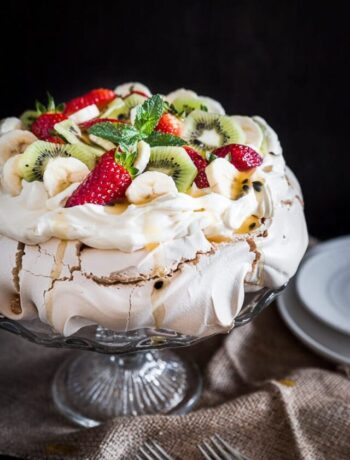 Large pavlova on a cake stand with serving plates nearby.