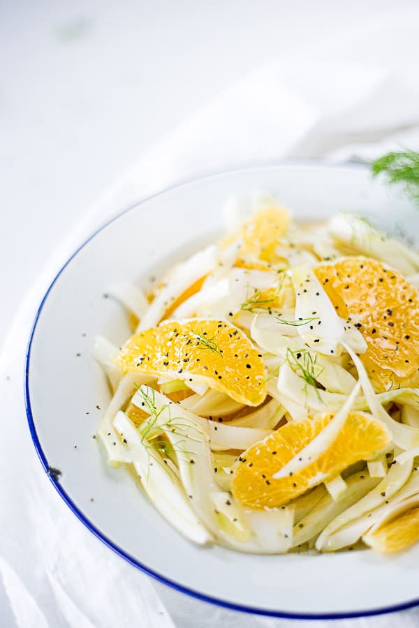 Sliced fennel and orange in a bowl, sprinkled with cracked black pepper and garnished with fennel leaves.