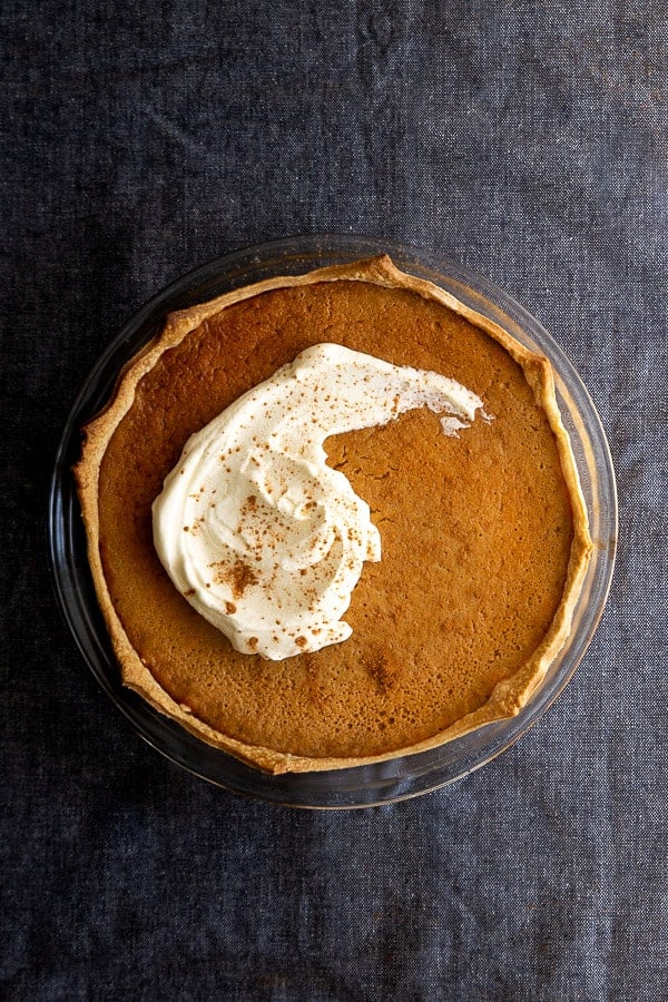 Whole pumpkin pie with coconut topped with slathering of cream.