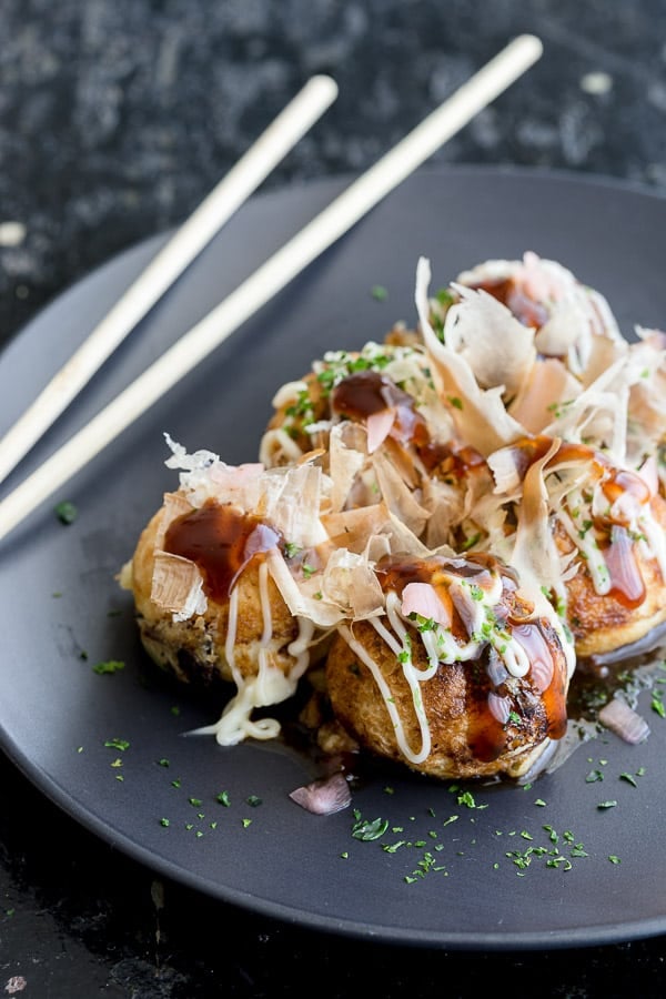 Plate of takoyaki balls topped with homemade takoyaki sauce, kewpie mayonnaise, aonori and katsuoboshi.