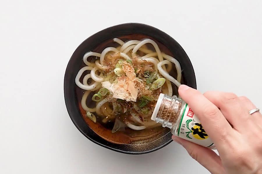 Sprinkling Japanese chilli flakes over the top of udon noodle soup.