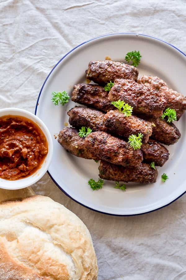 A plate of sausages next to ajvar dipping sauce and fresh bread.