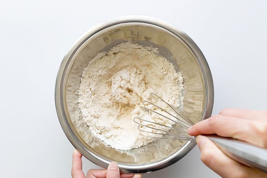 Mixing of crumpet batter with whisk in a bowl.