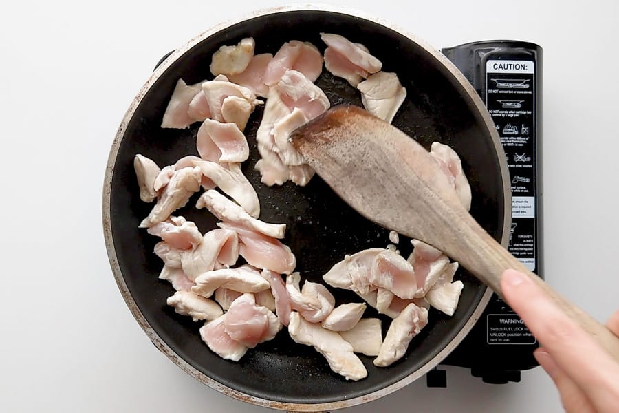 Frying thinly sliced chicken pieces in oil.