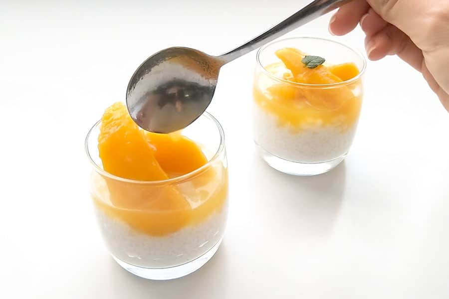 Adding a spoonful of mango syrup to the sago pudding bowls.