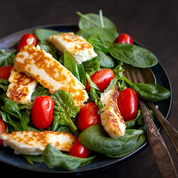 Haloumi salad in a bowl with serving fork and spoon.