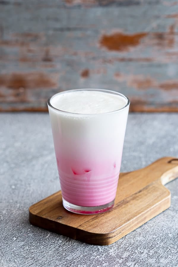 Glass of pink milk on wooden serving board.