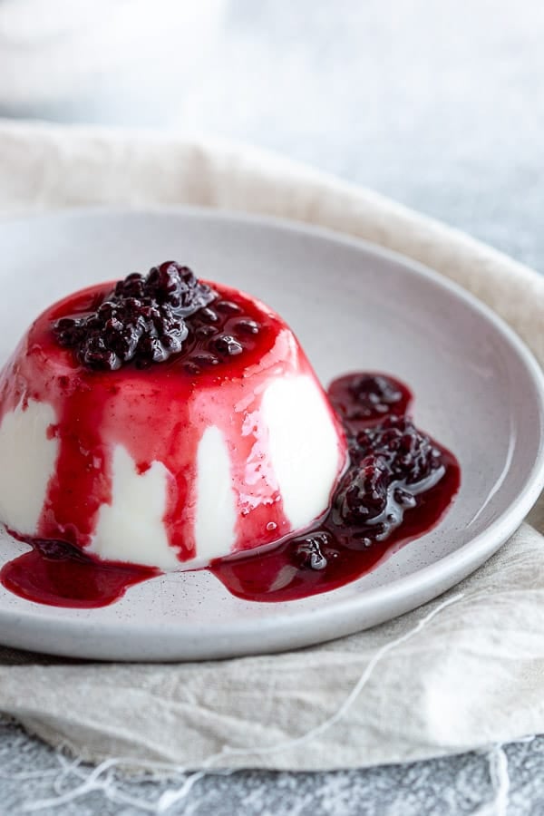 Blanc manger pudding on a plate with blackberry coulis drizzled on top.