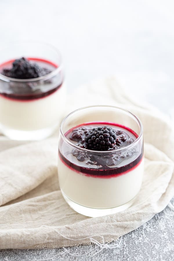 Two glasses of blancmange topped with blackberry coulis.
