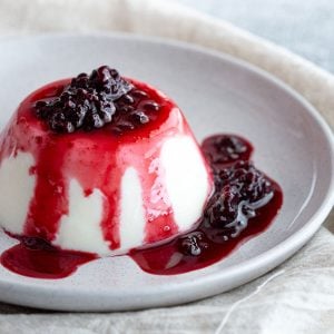 Blancmange set on a plate with blackberry coulis.