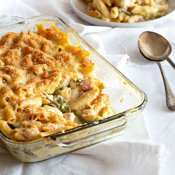 Oven dish full of creamy chicken pasta bake with serving spoons.