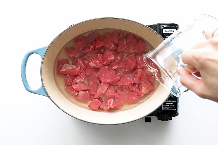 Pouring water over beef, ready to boil.