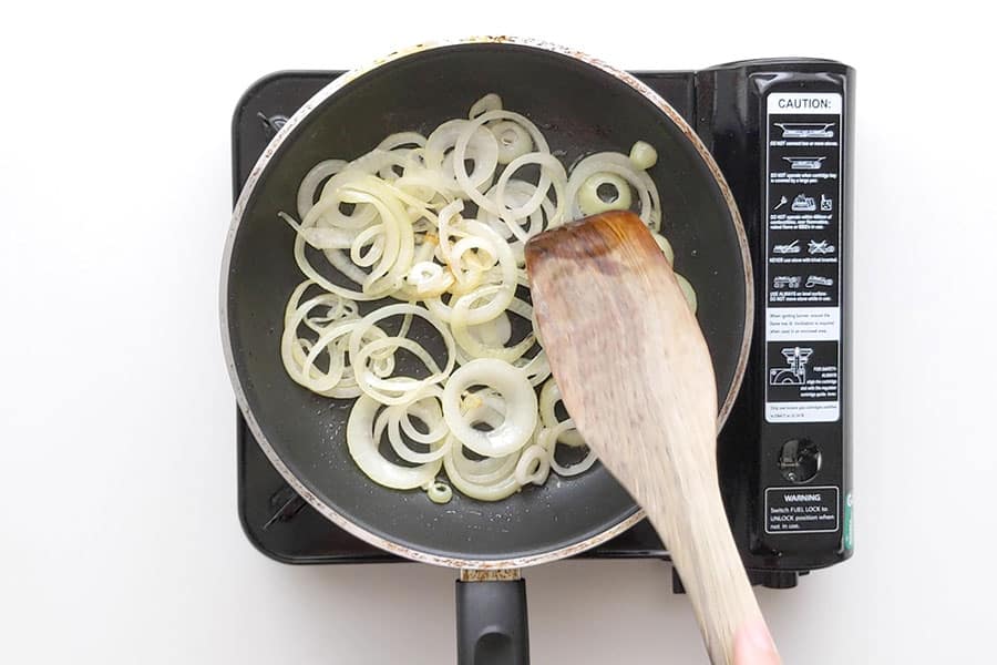 Onions slowly cooking in a medium frying pan.
