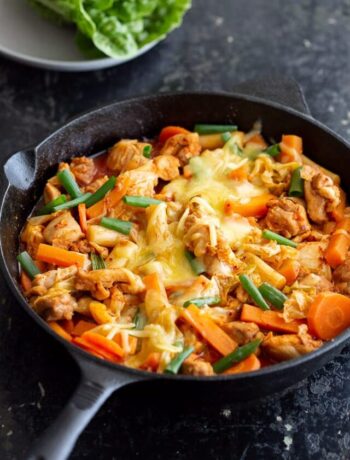 Korean spicy chicken stir fry in cast iron pot, topped with melted cheese.