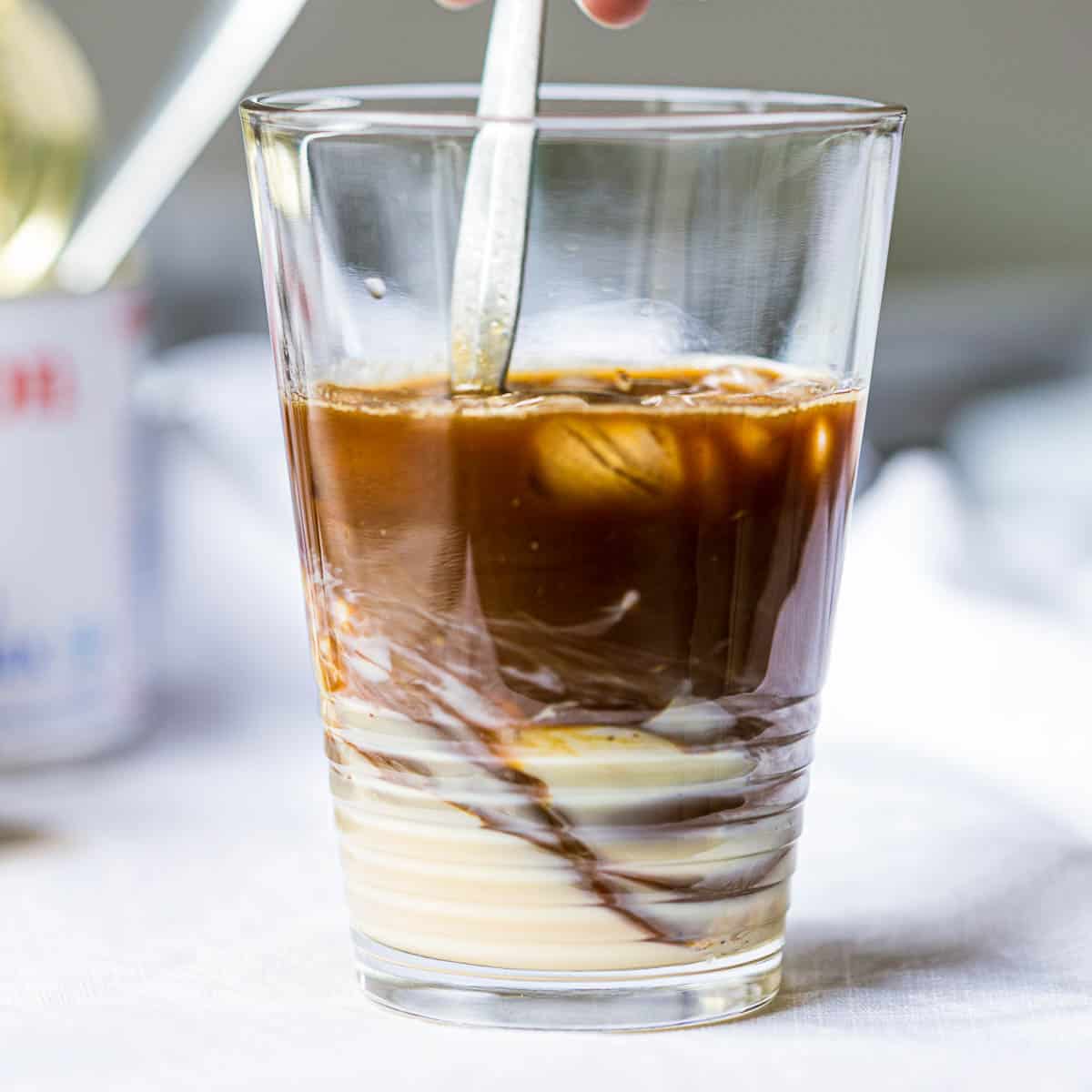Swirling Vietnamese coffee with condensed milk in a glass.