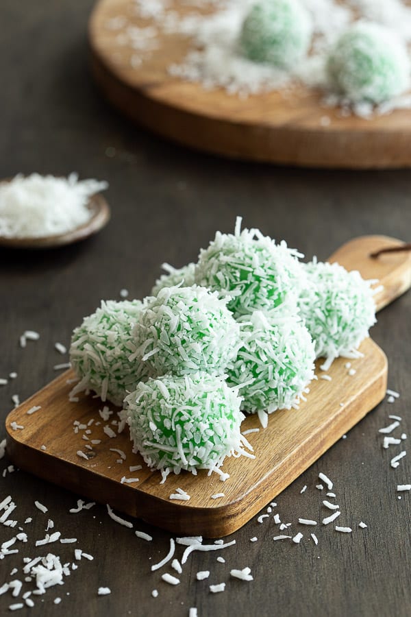 Stack of fresh klepon on wooden serving board with shredded coconut.