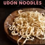 Pile of udon on wooden board with text overlay.
