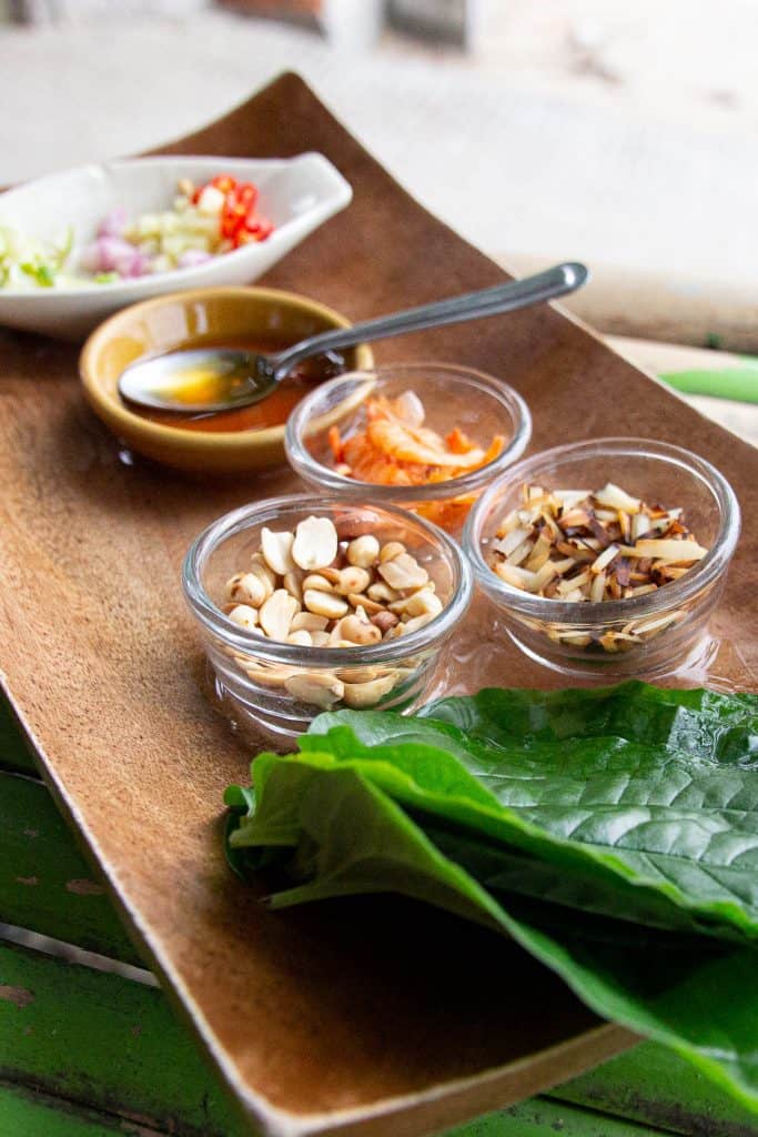 Miang kham ingredients on a platter next to a stack of betel leaves.