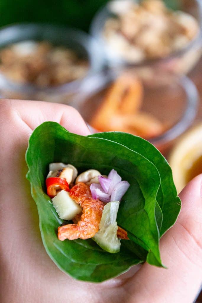 Holding a betel leaf folded into a cone shape, stuffed with fresh Thai ingredients.