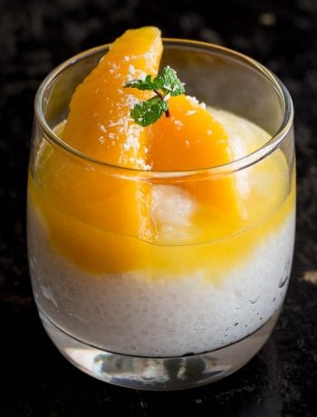 A glass jar filled with sago pudding, topped wth mango and syrup.