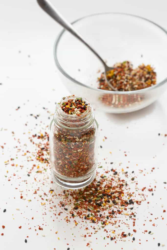 Overflowing jar of shichimi togarashi with bowl in background.