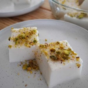 Two slices of Lebanese milk pudding dessert on a plate, garnished with crushed pistachios.
