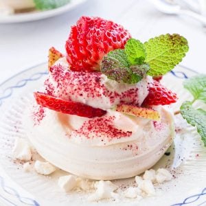 A mini eton mess pavlova on a plate with fruit, cream and crumbled meringue garnish.
