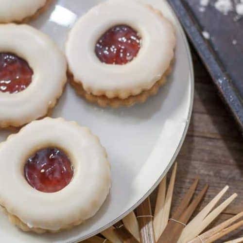 Shortbread cookies on a plate, filled with jam and topped with icing.