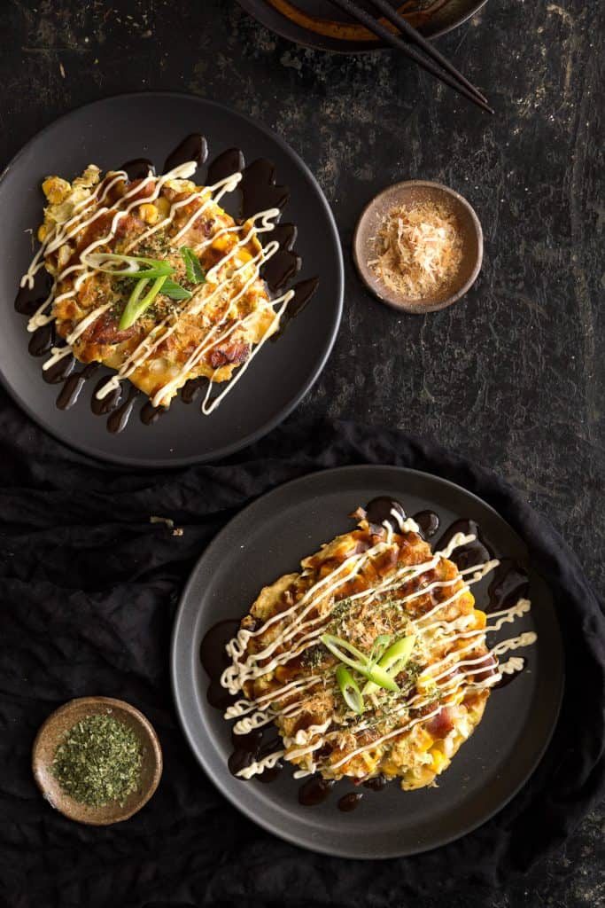 Top down of two Japanese savoury pancakes with sauces and toppings.