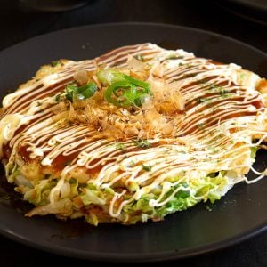 Okonomiyaki topped with sauce, kewpie mayonnaise, bonito flakes and seaweed flakes.