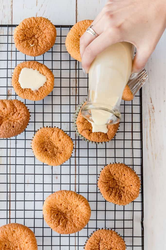 Pouring three milk syrup on top of freshly baked cupcakes.