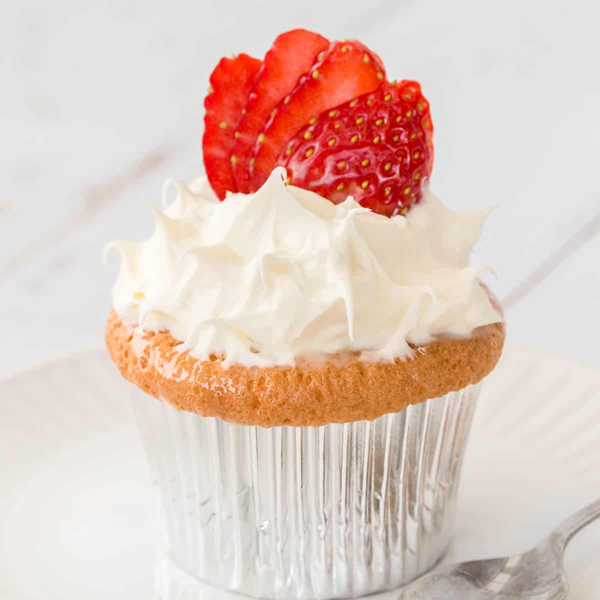 A baked cupcake in a foil patty pan, topped with whipped cream and strawberries
