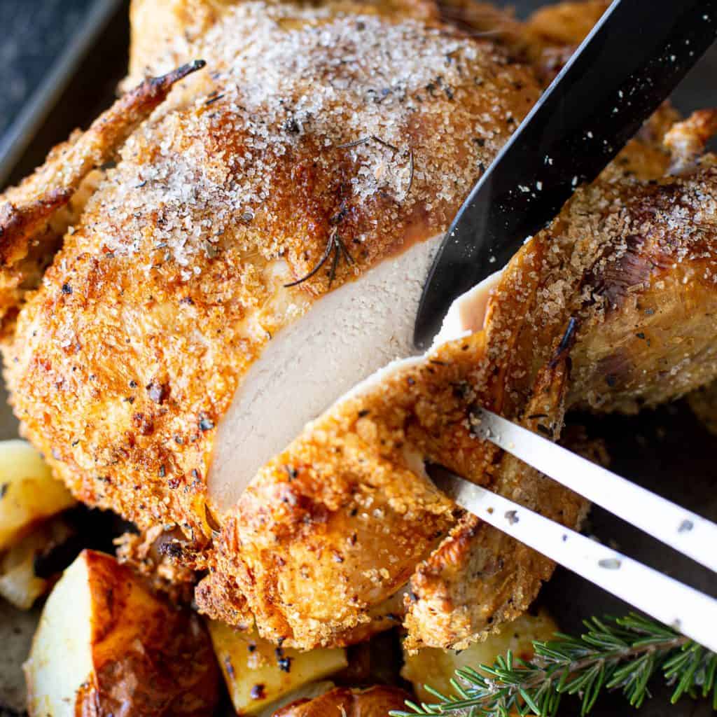 Slicing into a roast chicken with crispy skin.