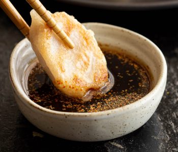 Gyoza being dipped into sauce with chopsticks.
