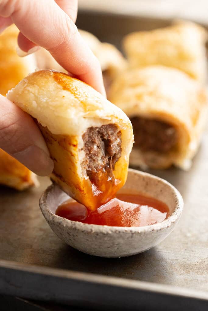 Dipping a sausage roll into tomato sauce.